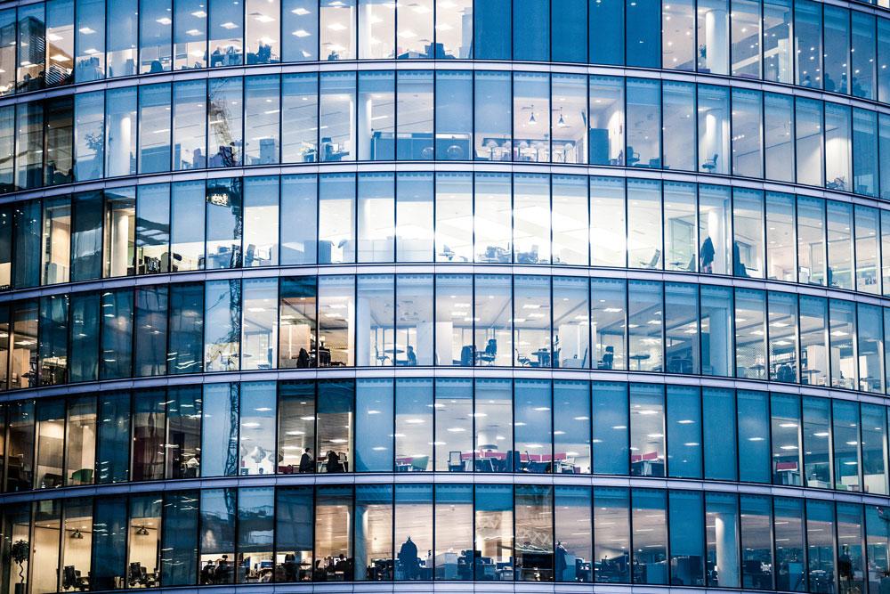 Glass front of office tower revealing activity inside.