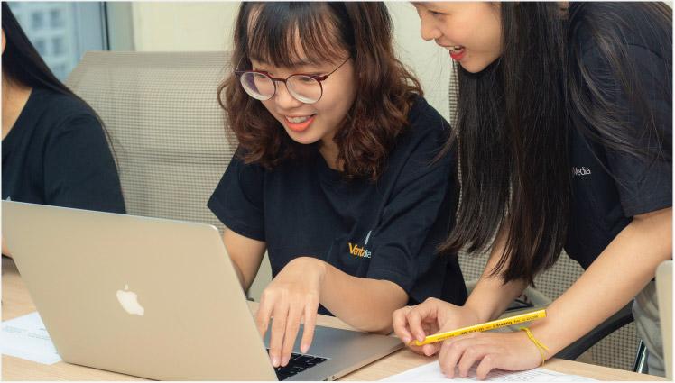 Person typing on laptop with colleague looking at screen smiling 