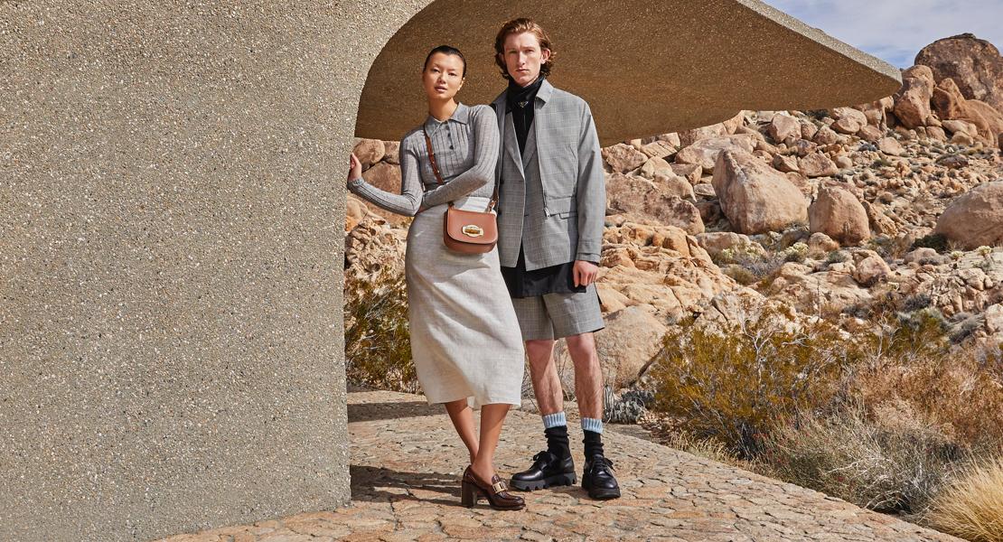 Two models stand in neutral-coloured luxury clothes in a desert landscape.