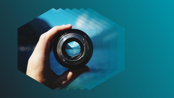 Photo of a hand holding a camera lens, inside a hexagon