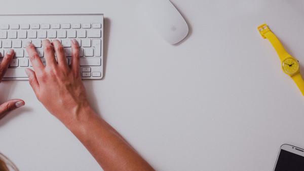 Hands typing on a keyboard with a watch and a cellphone to the side