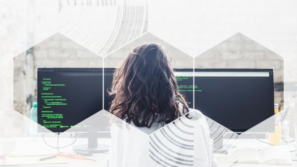 Photo of an engineer looking at code on two screens, viewed through three hexagons