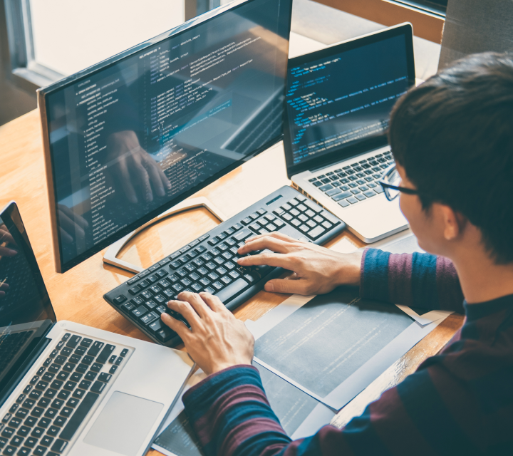 Person sitting at a computer with several laptops next to them